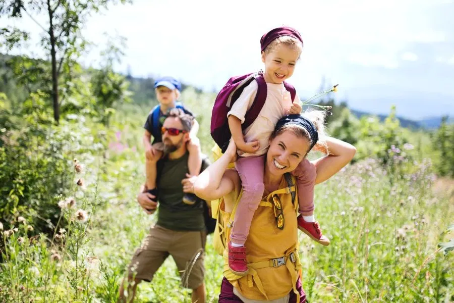 A mother and father hiking through the forest with their kids on their shoulders.